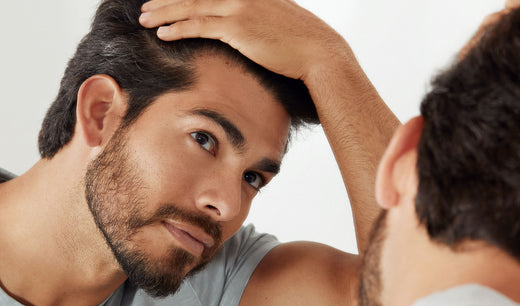 Young man looks in mirror at his first grey hair