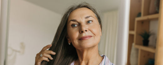 Smiling older woman looks at her aging and grey hair