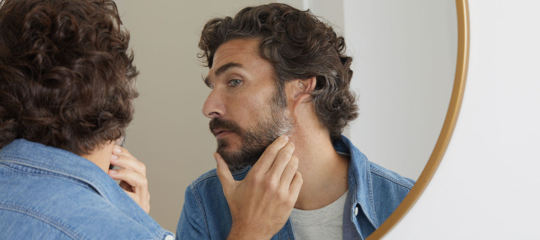 Man looks in mirror at grey hair in his beard