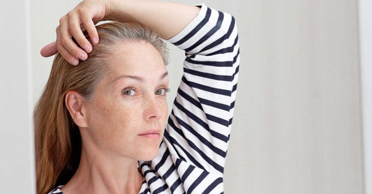 Menopausal woman looking at grey hair in mirror