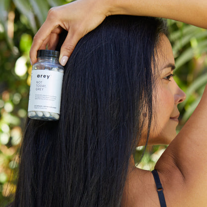 Woman with long healthy hair holding a bottle of Not Today Grey