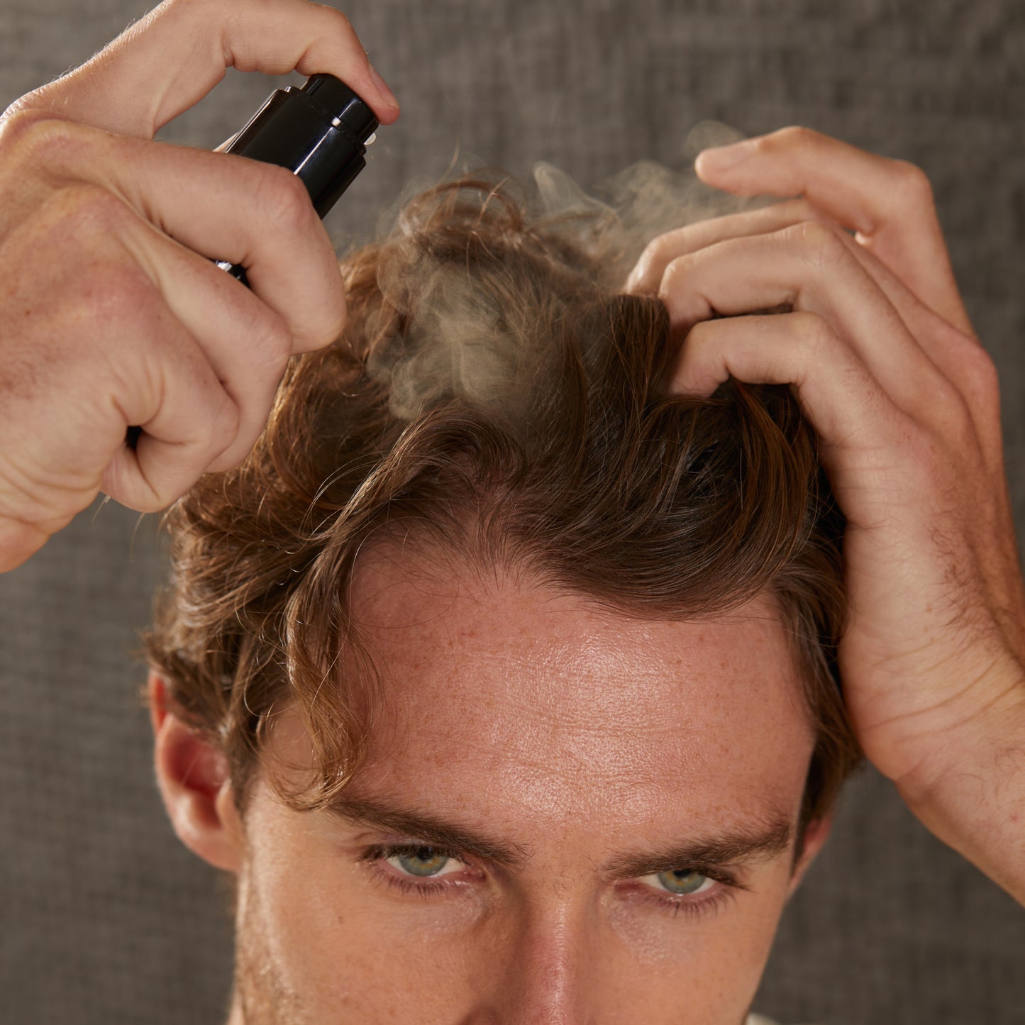 A man spraying Wait A Sec into his hair